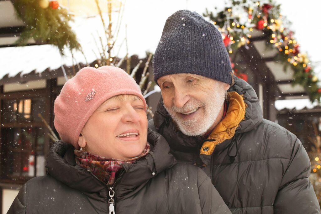 Home Joyful elderly couple enjoying a snowy winter day outdoors, dressed warmly in winter clothing.